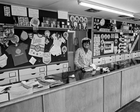 A woman smiles behind a counter in the Leeds United souvenir shop, surrounded by merchandise