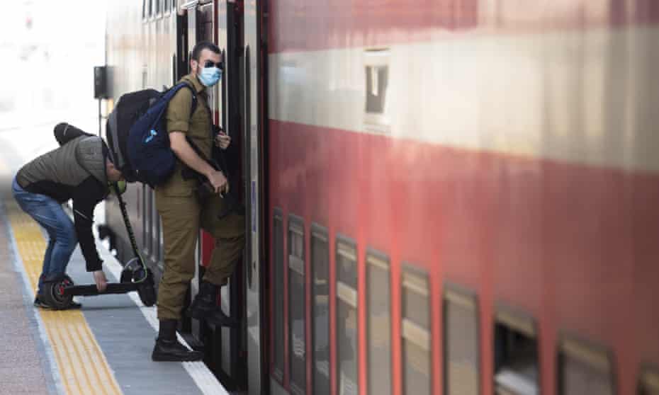 a young israeli soldier boards a train in tel aviv wearing face mask
