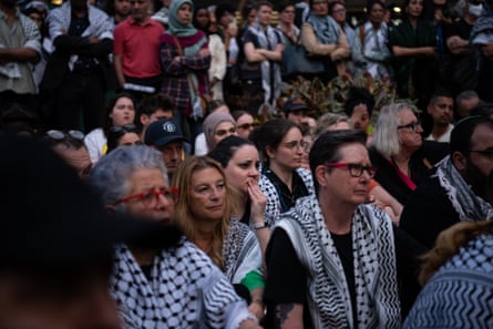 People draped in keffiyehs attend a vigil in the city