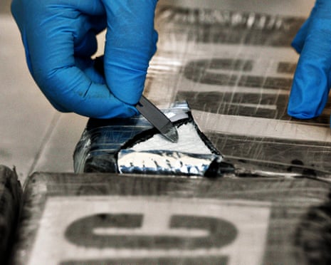 Gloved fingers scooping a bit of white powder from clingfilm-wrapped packages