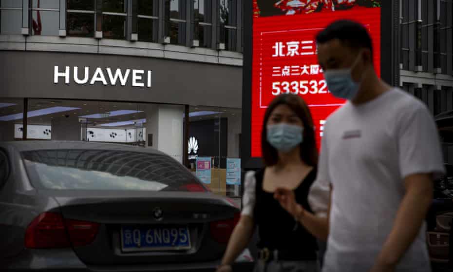 People wearing face masks walk past a Huawei store in Beijing, China
