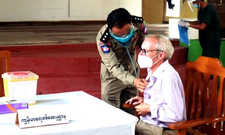 Sean Turnell is sitting in a chair wearing a mask and appears to be having his heart checked by a Myanmar official using a stethoscope on his chest