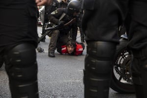 A man looks towards the camera as a riot police officer holds him on the floor with hands cuffed behind his back