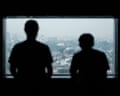 Two Indonesian former scam trafficking victims stand silhouetted at a window overlooking a hazy city