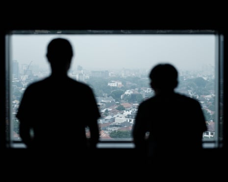 Two Indonesian former scam trafficking victims stand silhouetted at a window overlooking a hazy city