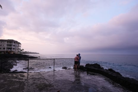 Ryanna and Jim Fry stand at a fence looking out over the ocean under a cloudy sky