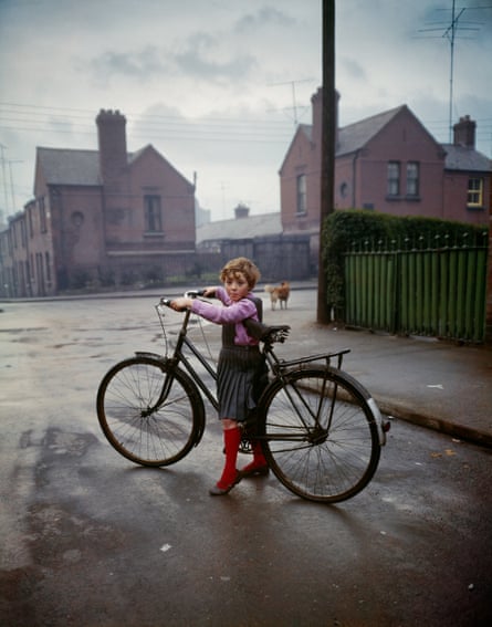 A small girl with a big bike near a crossroads of residential streets with a dog in the background