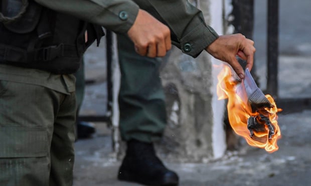 A member of the Bolivarian National Guard burns a copy of amnesty measures for anyone in the military who disavows Maduro