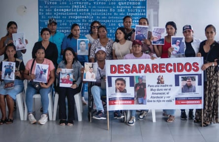 About 20 people, mostly women, hold up pictures of young men next to a big banner saying ‘Desaparecidos’