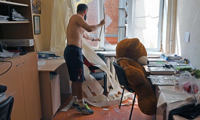 A teacher removes broken glass from an office in a public school following an air strike in Kharkiv on Saturday.