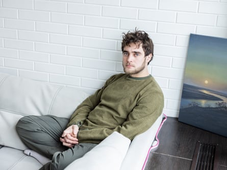 A young bearded man sits connected a sofa pinch a scenery coating beside him
