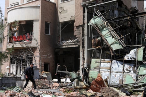 Two men walk past the bomb-damaged Shahid Beheshti University building in Tehran, with rubble scattered outside