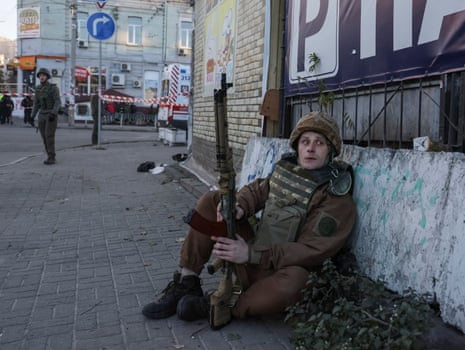 A Ukrainian serviceman sits in the street after a Russian drone strike.