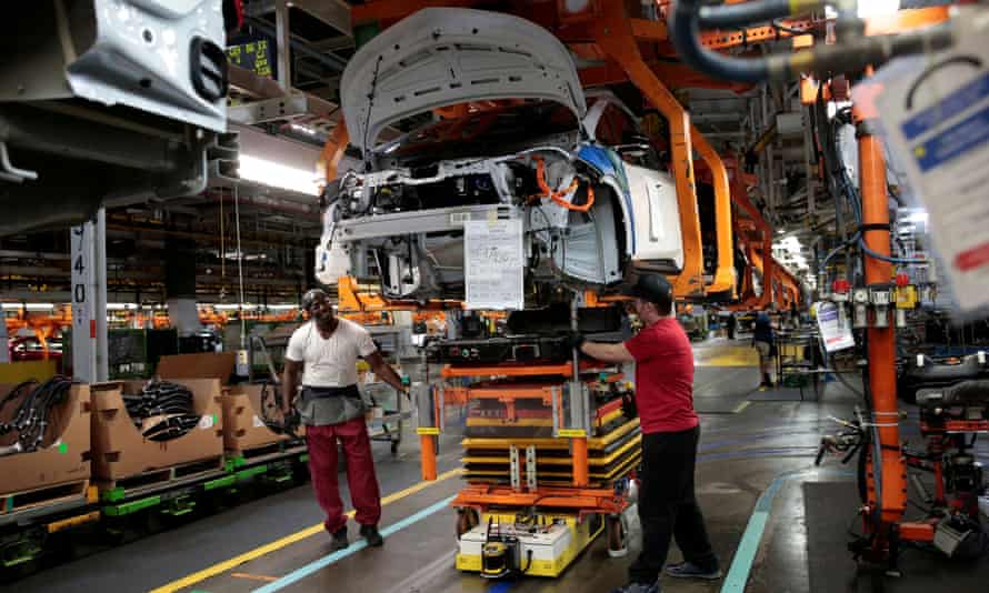 GM assembly workers connect a battery pack under a partially assembled Chevrolet Bolt EV vehicle