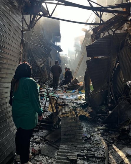 People stand in a narrow alley surrounded by twisted and blackened metal and debris.