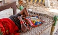 A woman rests on a wicker bed with a fan covering her face