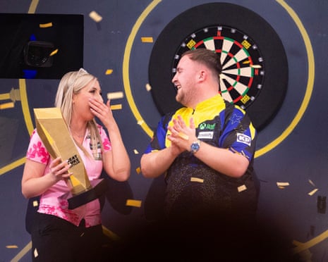 Fallon Sherrock holds her trophy with a hand over her mouth as she smiles at Luke Littler who is clapping.