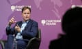 Nick Clegg gesticulates as he speaks; he is sitting in a black leather chair against a purple backdrop with white Chatham House logos; he faces a shadowy head and shoulders in the foreground