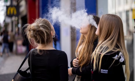 Young people standing outside shops using single-use vaping products.