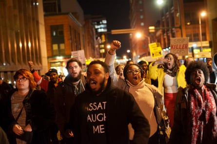 Protesters march outside at night, raising their fists and chanting or yelling.