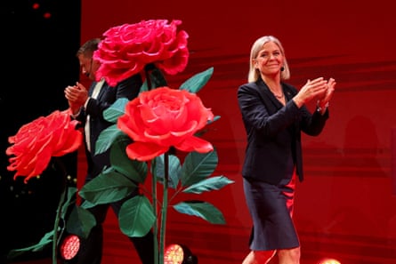 Magdalena Andersson on stage at a political event, with roses in the foreground as she applauds