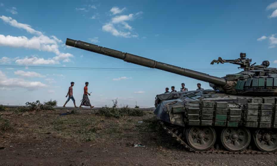 Civilians walk past an abandoned tank in southern Tigray