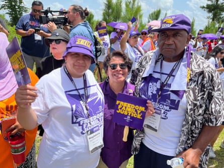 two women next to a man, all wearing SEIU gear, attending a rally outside