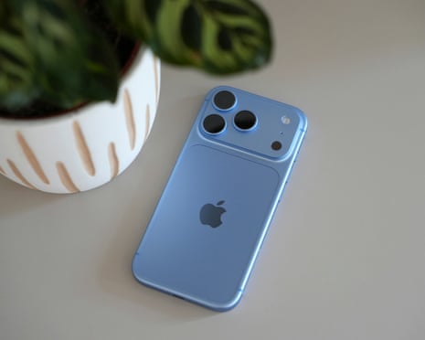 A light blue iPhone 18 Pro with triple camera lenses lies face-down on a table near a plant