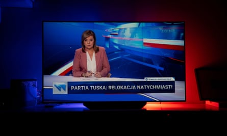 A TVP newsreader seen on a TV in a dimly lit living room or lounge