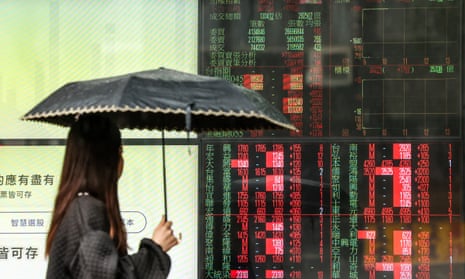 A woman walks past a screen showing share prices of the Taiwan stock market in Taipei.