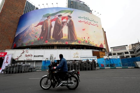 A man on a motorcycle looks at a large billboard featuring Iran’s new supreme leader Mojtaba Khamenei and late supreme leaders Ali Khamenei and Ruhollah Khomeini in Tehran, Iran