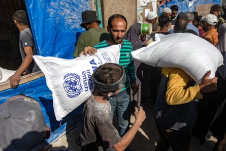 Palestinian men lift large white sacks of flour, which have blue UN logos on them, out of a truck and carry them away.