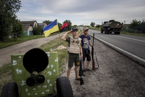 Maksym and Andrii, 11, salute to Ukrainian soldiers, holding plastic guns, as they play at the self-made checkpoint on the highway in Kharkiv region, 20 July.