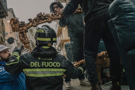 A firefighter helps people carry a large, ornate gold-framed mirror