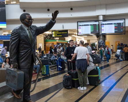 Passengers at an airport, with a man standing in the forefront, waving
