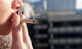 Young woman with fingernails painted purple smoking outdoors with sun on her face: a close-up showing her holding a cigarette in her mouth