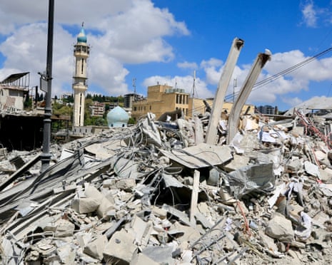 Rubble and broken concrete fill the foreground with a mosque minaret and dome visible among damaged buildings in Nabatieh