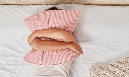 Top view of a beautiful young woman lying in bed covering her face with a pillow.