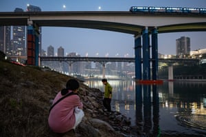A dusk shot of couple the river’s edge with bridges and skyscrapers behind them