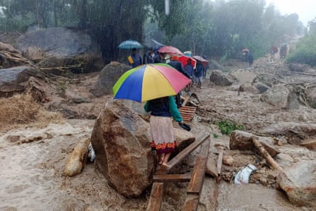 People walk across a makeshift bridge over flood water in Blantyre after a cyclone in 2023.