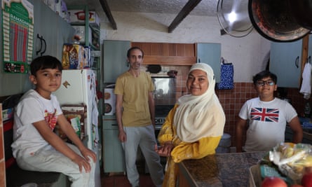 The family in their kitchen. A young boy sits on a worktop while a man, woman and another, slightly older boy stand around the room.