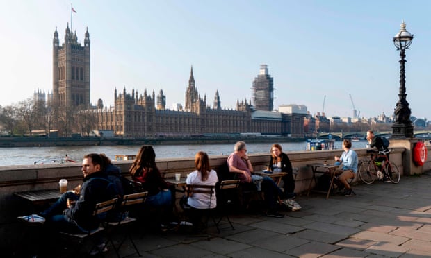 People sitting by the River Thames opposite the Houses of Parliament.