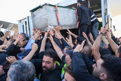 Πάνω από δώδεκα άντρες απλώνουν το χέρι για να αγγίξουν το φέρετρο καθώς ξεφορτώνεται ένα όχημα.