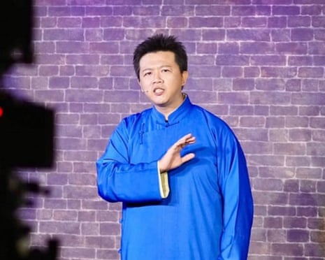 Comedian Huang Yi-hao, in a blue traditional jacket, gestures while speaking on stage