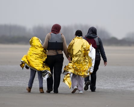 Two women walk away from the camera, accompanying two children wrapped in gold foil blankets