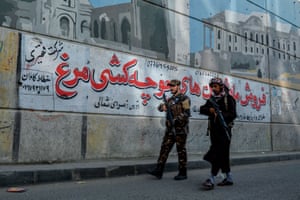 Taliban fighters patrol a road against the backdrop of a mural painted on a wall in Kabul on 26 September.