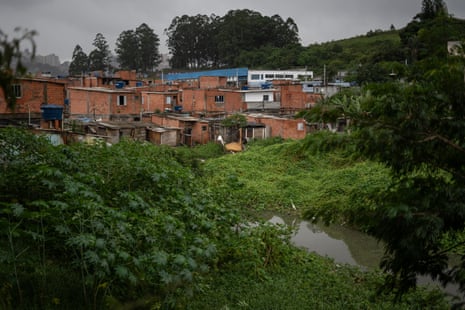 A small stream flows in front of a group of informal houses surrounded by trees.