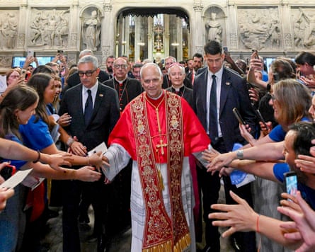 Pope Leo holds his hands out to greet people on either side of him at a cathedral