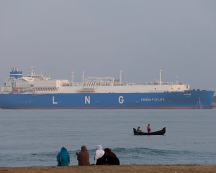 A large vessel with blue hull and the letters LNG in white in the distance, and people on a beach in the foreground