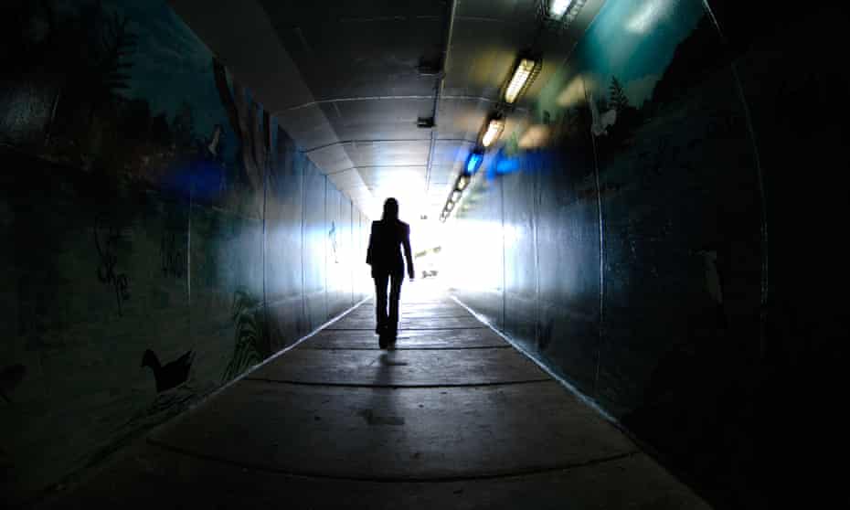 A woman walking through a dark tunnel alone